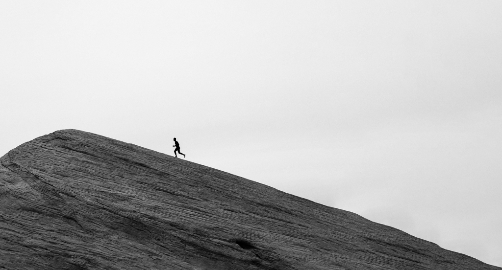 Schwarz-Weiß-Foto einer Person die einen Berg hoch rennt.