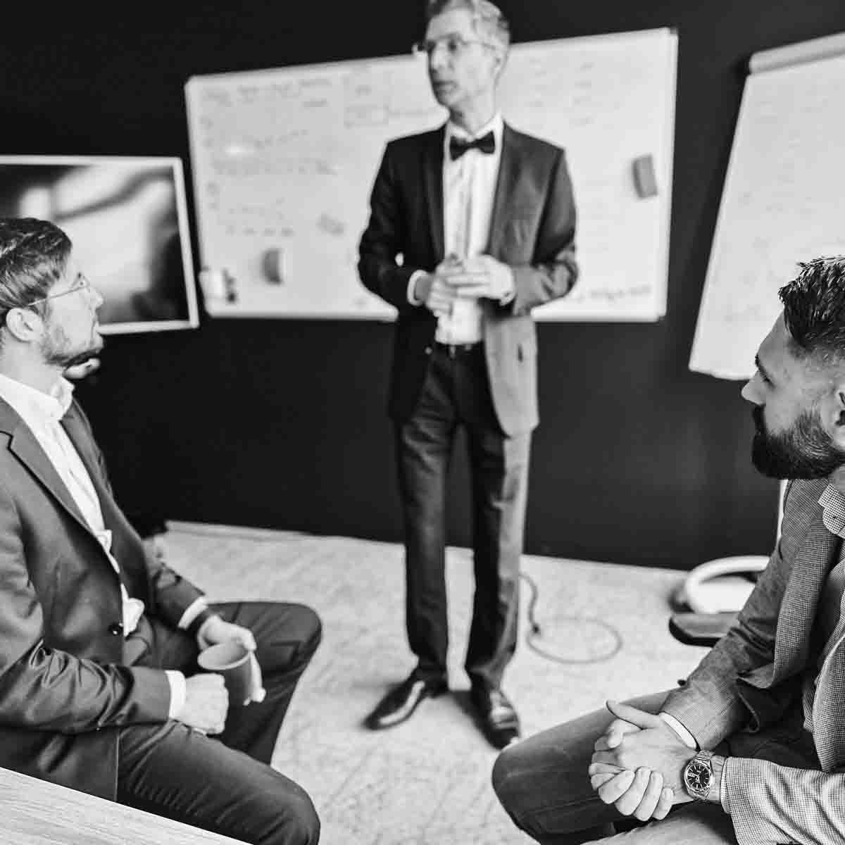 Schwarz-Weiß-Foto von drei BCxP-Mitarbeitern in Anzügen, die sich in der Stuttgarter Niederlassung unterhalten.
