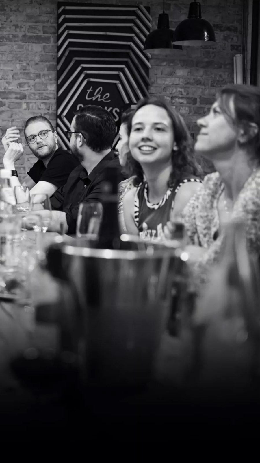 Ein Schwarz-Weiß-Foto einer Gruppe von Mitarbeiter:innen an einem Tisch, bei einem gemütlichen Teamabendessen gemeinsam.