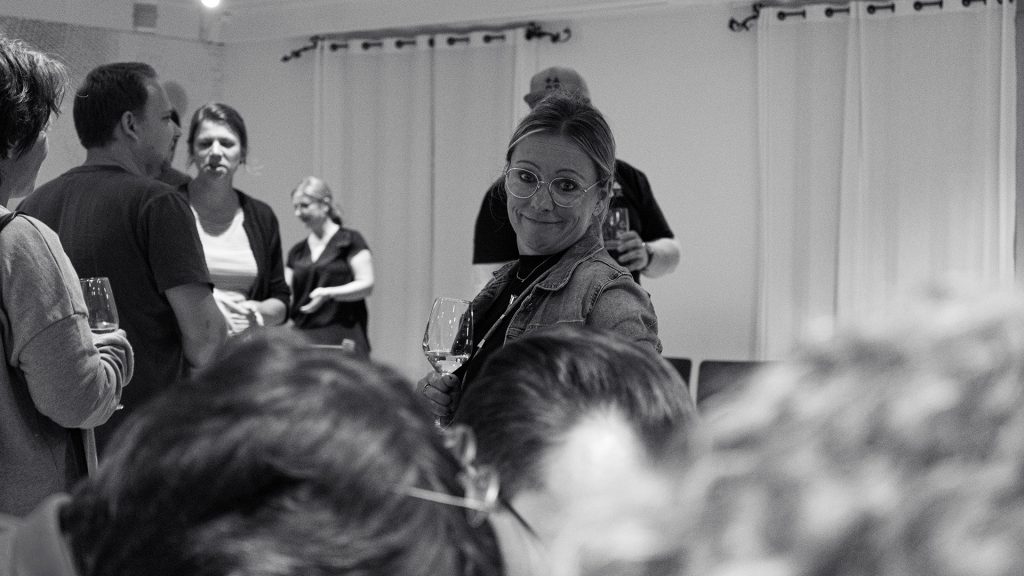 Ein Schwarz-Weiß-Foto einer Frau, die in die Kamera lächelt und um die herum eine Gruppe von Menschen in einem Raum steht.