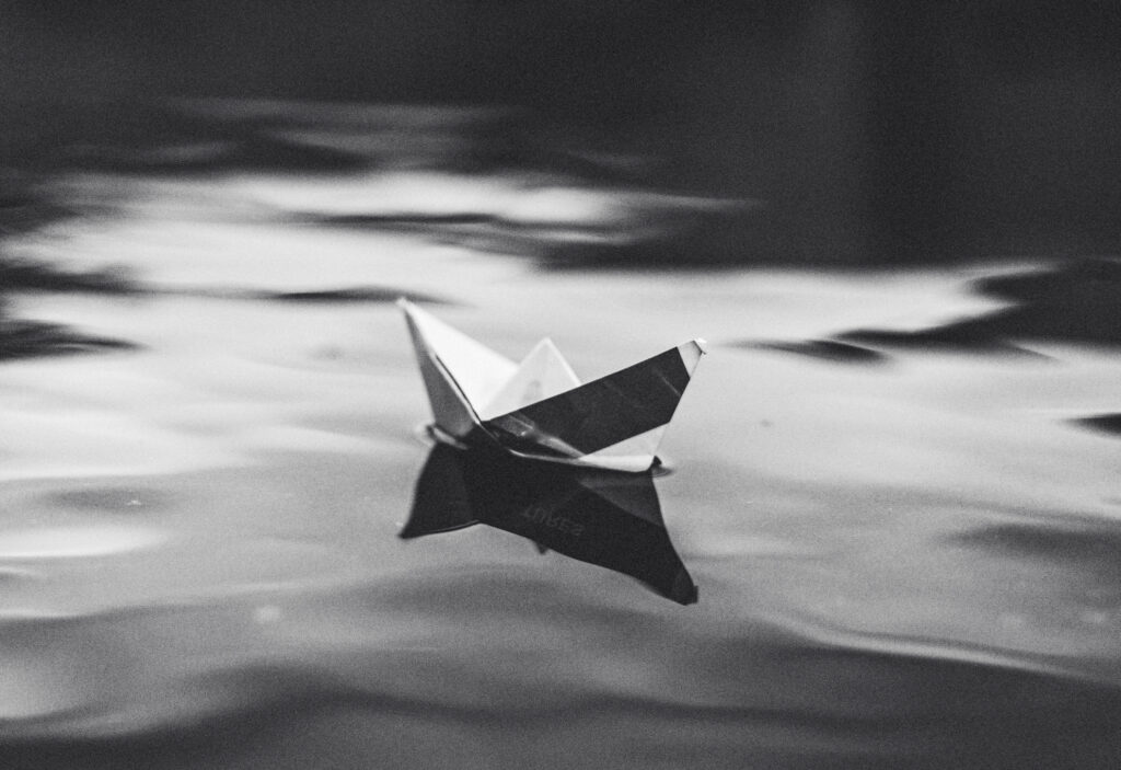 Ein Schwarz-Weiß-Foto eines im Wasser schwimmenden Origami-Bootes.