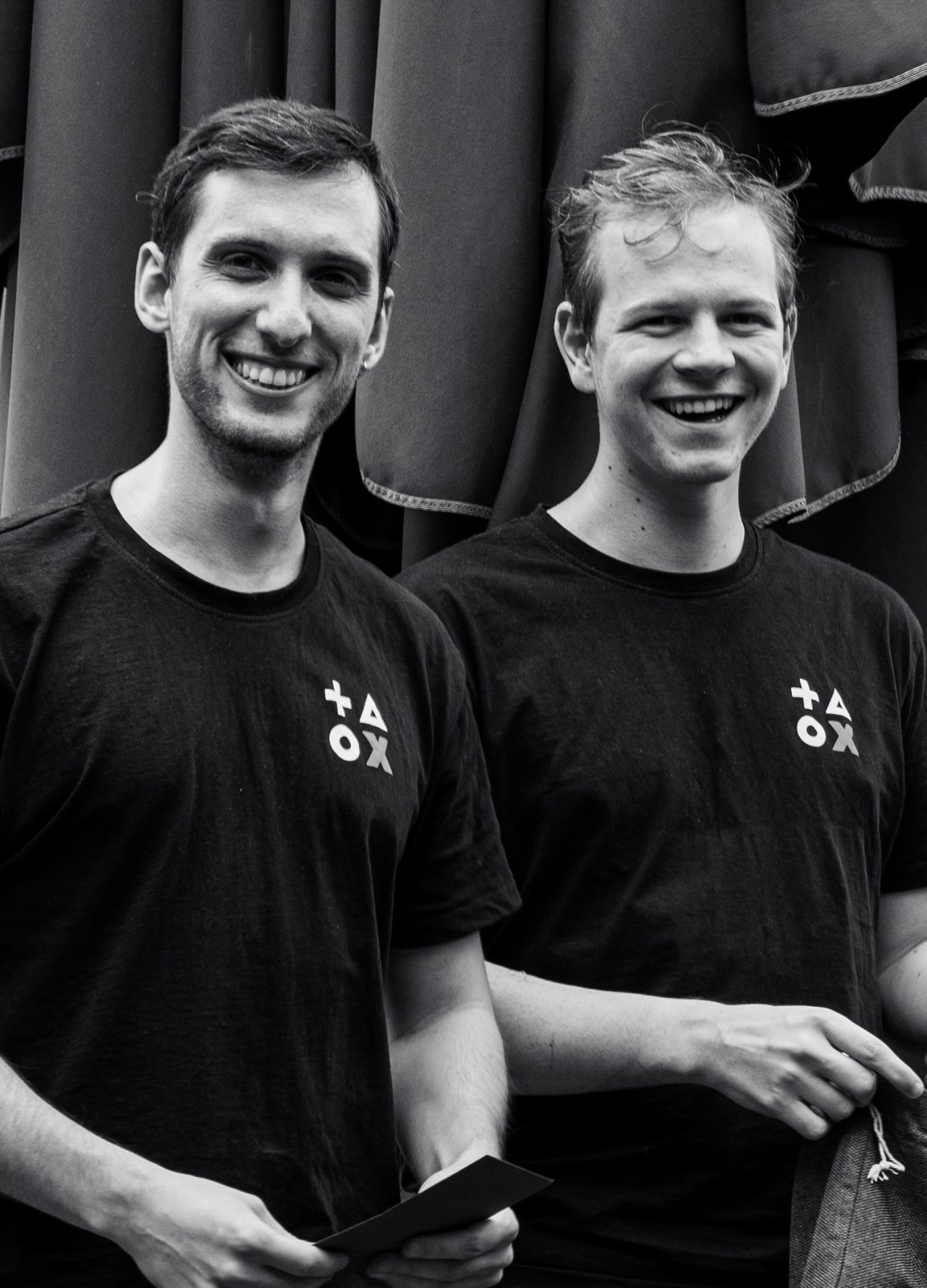 Ein Schwarz-Weiß-Foto zweier Männer in schwarzen T-Shirts, die nebeneinander stehen und lachen.