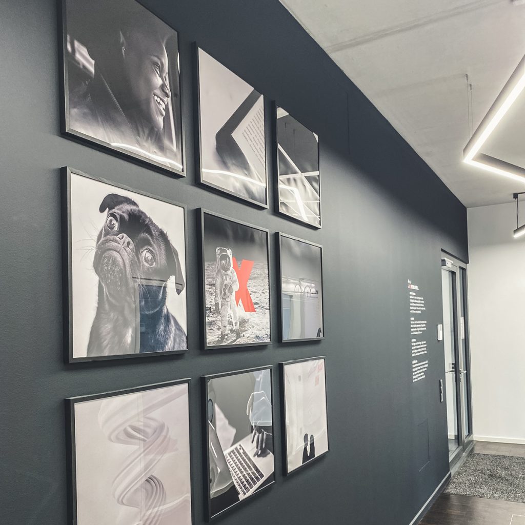 Eine Sammlung gerahmter Schwarz-Weiß-Fotografien, die an einer grauen Wand in einem modernen Innenraum ausgestellt sind.