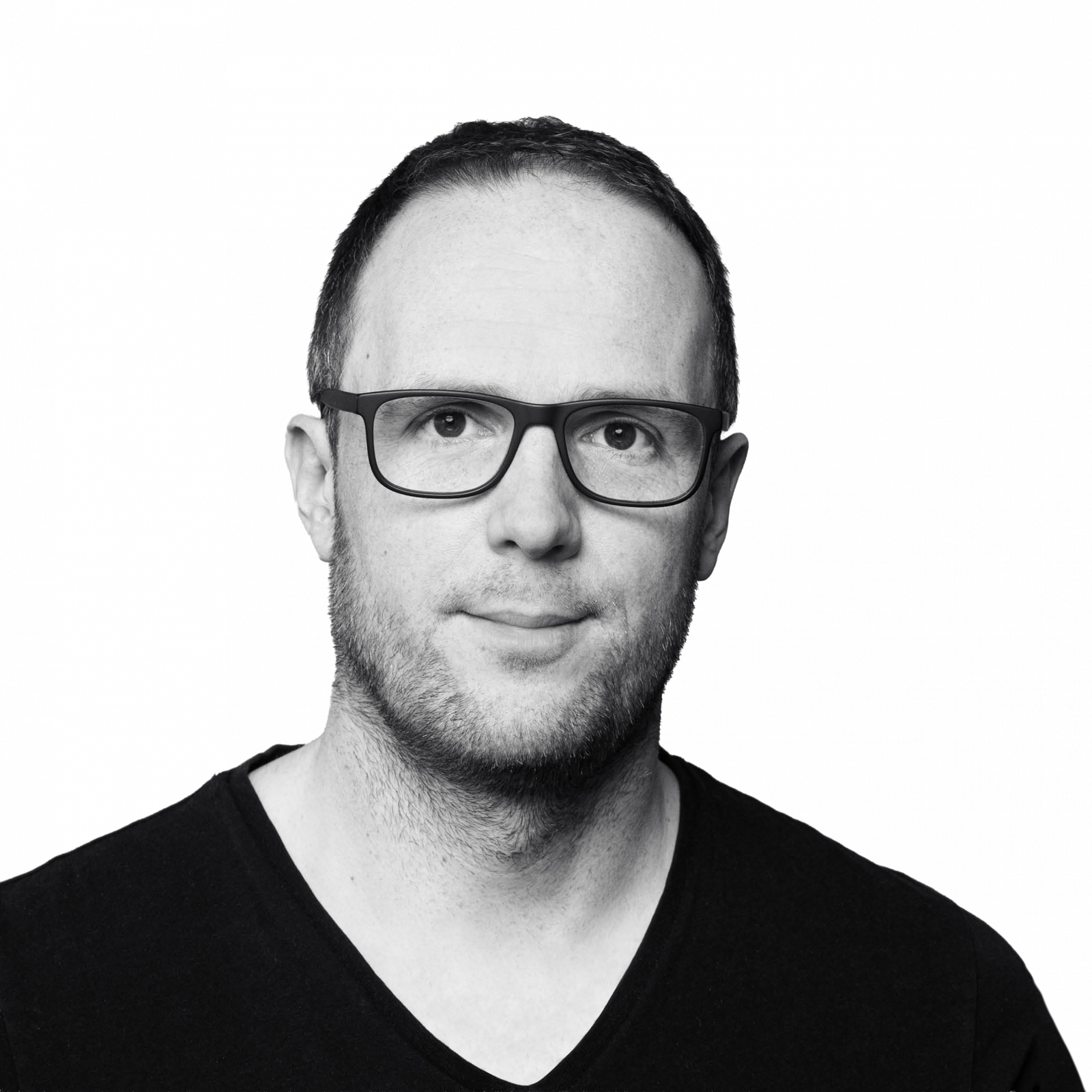 Ein Mann mit kurzen Haaren, Brille und gestutztem Bart, der ein schwarzes Hemd mit V-Ausschnitt trägt, ist vor einem schlichten weißen Hintergrund abgebildet.