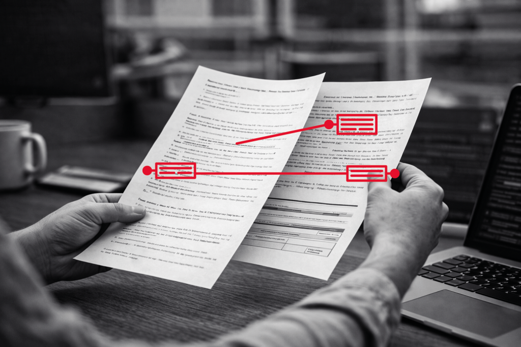 Eine Person hält zwei gedruckte Dokumente mit roten Markierungen, die entsprechende Textabschnitte zwischen den Seiten hervorheben; im Hintergrund sind ein Laptop und eine Kaffeetasse zu sehen.